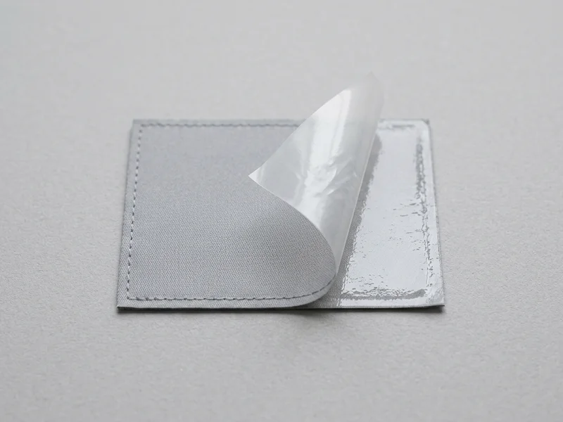 Patch mit halb abgezogener Schutzfolie — die selbstklebende Rückseite liegt frei